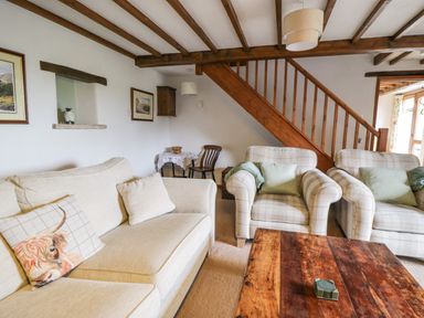 A living room with a beige sofa and two armchairs near a wooden coffee table and staircase at Daisy Cottage in Penruddock