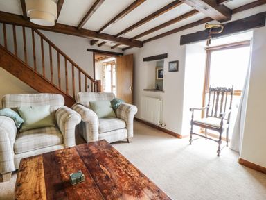 A sitting room with two armchairs a wooden coffee table a wooden stair railing and a wooden chair near a window at Daisy Cottage in Penruddock