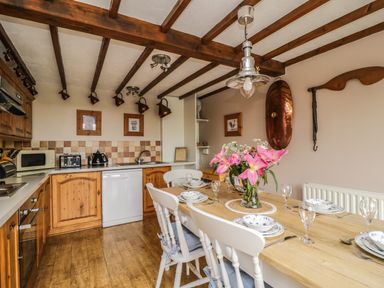 A kitchen with wooden cabinets a dining table set with plates and glasses and flowers at Daisy Cottage in Penruddock
