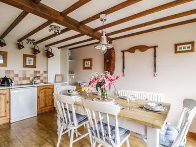 A kitchen and dining area with a wooden table set with plates glasses and a vase of flowers at Daisy Cottage in Penruddock