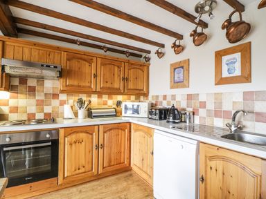 A kitchen with wooden cabinets tiled backsplash and appliances at Daisy Cottage Penruddock