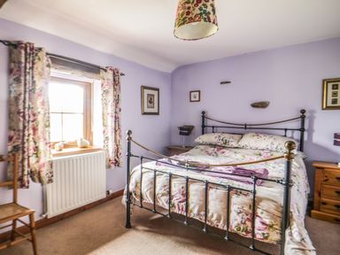 A bedroom with a metal bed frame floral bedding wooden furniture and floral curtains at Daisy Cottage in Penruddock