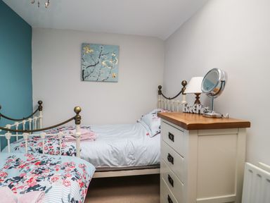 A bedroom with two single beds a chest of drawers with a mirror and lamp and a butterfly picture on the wall at Daisy Cottage in Penruddock
