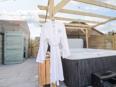 An outdoor patio with a hanging white robe a wooden pergola and a hot tub at Daisy Cottage in Penruddock
