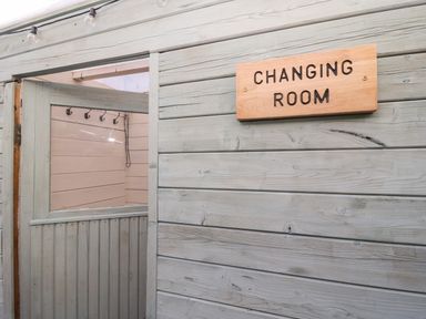 An open wooden changing room door with hooks inside and a wooden changing room sign outside at Daisy Cottage in Penruddock