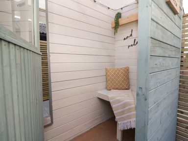 A small wooden seating nook with a bench, yellow cushion, and striped blanket at Daisy Cottage in Penruddock