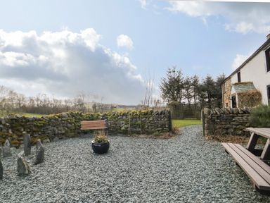 An outdoor garden area with a wooden bench stone wall and gravel ground at Daisy Cottage in Penruddock