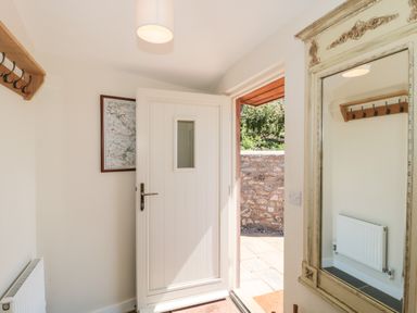 An entryway with a white door open to a stone patio a large mirror and a wooden coat rack on the wall at Lilac Cottage in Wookey Hole near Wells