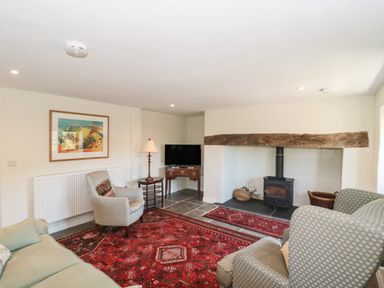 A living room with armchairs a wood burning stove and a red rug at Lilac Cottage in Wookey Hole near Wells