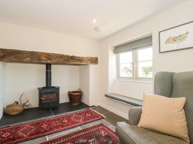 A sitting area with a wood-burning stove baskets a window seat and an armchair at Lilac Cottage in Wookey Hole near Wells