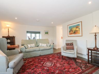 A living room with two armchairs a sofa a red patterned rug table lamps and framed artwork on walls at Lilac Cottage in Wookey Hole near Wells