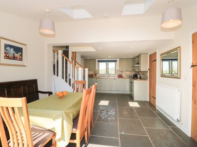 A kitchen and dining area with wooden chairs a table with a yellow tablecloth and a bowl of oranges at Lilac Cottage in Wookey Hole near Wells
