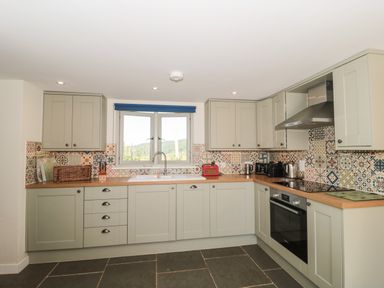 A kitchen with light grey cabinets patterned tile backsplash and a window at Lilac Cottage in Wookey Hole near Wells