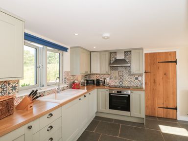 A kitchen with cabinets a wooden countertop a sink and patterned tile backsplash at Lilac Cottage in Wookey Hole near Wells