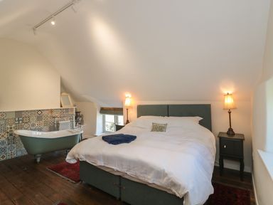 A bedroom with a double bed bedside lamps a bathtub and patterned wall tiles at Lilac Cottage in Wookey Hole near Wells