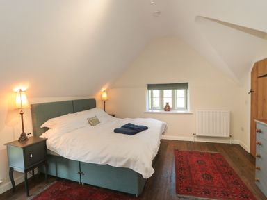 A bedroom with a double bed bedside tables lamps rugs and a small window at Lilac Cottage in Wookey Hole near Wells