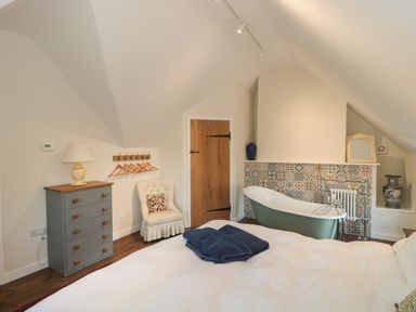 A bedroom with a dresser chair bathtub and tiled wall at Lilac Cottage in Wookey Hole near Wells