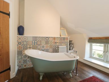 A bathroom with a green freestanding bathtub and patterned tiles behind at Lilac Cottage in Wookey Hole near Wells