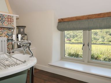 A bathroom with a freestanding bathtub near a window with a green blind at Lilac Cottage in Wookey Hole near Wells