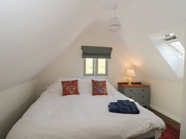 A bedroom with a double bed with red floral cushions a window a bedside table with a lamp and folded towels at Lilac Cottage in Wookey Hole near Wells