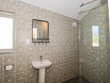 A bathroom with a pedestal sink a wall-mounted mirror a toilet paper holder and a shower area at Lilac Cottage in Wookey Hole near Wells