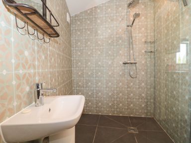 A bathroom with a sink a shower and patterned tiled walls at Lilac Cottage in Wookey Hole near Wells