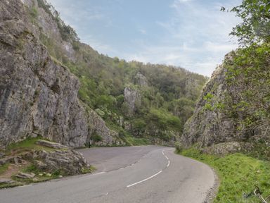 A road curving between rocky cliffs with greenery and trees at Lilac Cottage in Wookey Hole near Wells
