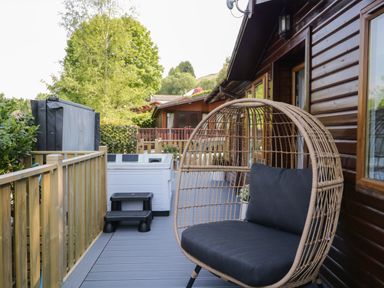 An outdoor deck with a hanging wicker chair and a hot tub at Broad Oak Lodge in Applethwaite 7 Limefitt Park near Windermere