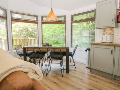 A dining area with a wooden table and black chairs near windows and a kitchen counter at Broad Oak Lodge in Applethwaite 7 Limefitt Park near Windermere