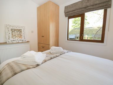 A bedroom with a bed towels on the bed a wooden wardrobe a window with a view of trees and a building at Broad Oak Lodge Applethwaite 7 Limefitt Park near Windermere