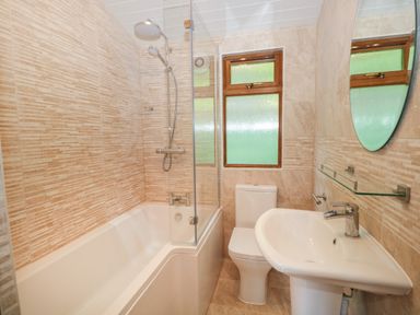 A bathroom with a bathtub shower combination a toilet a sink and a window at Broad Oak Lodge Applethwaite 7 Limefitt Park near Windermere