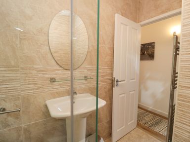A bathroom with a pedestal sink a round mirror a glass shelf and a partially open door at Broad Oak Lodge Applethwaite 7 Limefitt Park near Windermere