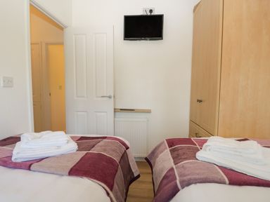 A bedroom with two single beds with towels on them a wooden wardrobe and a wall mounted tv at Broad Oak Lodge Applethwaite 7 Limefitt Park near Windermere