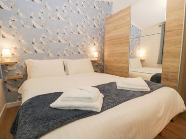 A bedroom with a double bed white linens folded towels bedside lamps and a wardrobe with a mirror Broad Oak Lodge Applethwaite 7 Limefitt Park near Windermere