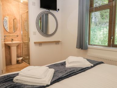 A bedroom with a bed dressed with folded towels near a window and a bathroom visible through an open door at Broad Oak Lodge Applethwaite 7 Limefitt Park near Windermere