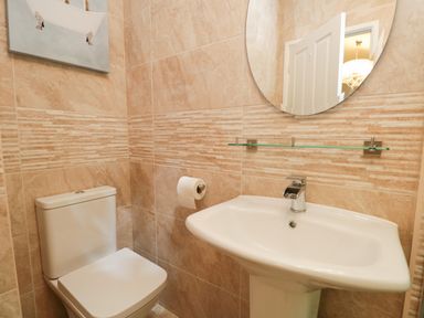 A bathroom with a toilet a sink wall-mounted glass shelf and a round mirror at Broad Oak Lodge Applethwaite 7 Limefitt Park near Windermere
