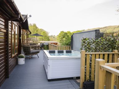 A deck with a hot tub egg chair table and umbrella outside a wooden cabin at Broad Oak Lodge Applethwaite 7 Limefitt Park near Windermere