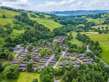 A cluster of wooden lodges in a green valley surrounded by trees and hills at Broad Oak Lodge in Applethwaite 7 Limefitt Park near Windermere