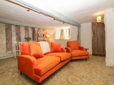 A living room with orange sofa and armchair patterned carpet and rustic wooden door at The Hideaway at Burrow Hill Ottery St Mary