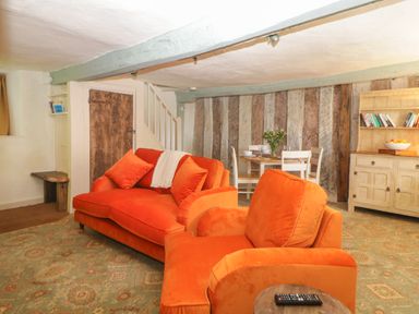 A living room with orange sofas a wooden dining table with chairs and a cabinet at The Hideaway at Burrow Hill Ottery St Mary