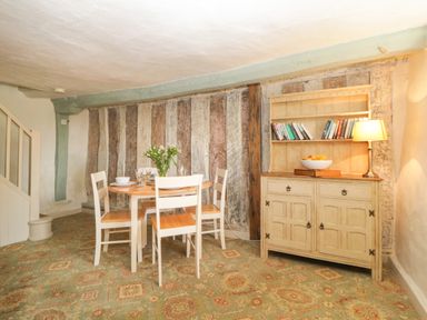 A dining room with a round table and four chairs a cabinet with a lamp and books and a patterned carpet at The Hideaway at Burrow Hill in Ottery St Mary