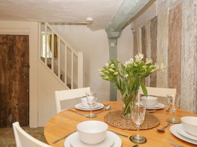 A dining area with a round wooden table set with white bowls plates cutlery and glasses and a vase of flowers at The Hideaway at Burrow Hill in Ottery St Mary