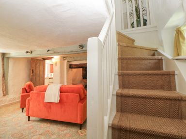 A small living room with orange sofas next to a staircase with a brown carpet at The Hideaway at Burrow Hill in Ottery St Mary