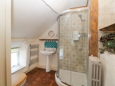 A bathroom with a glass shower enclosure a pedestal sink wooden toilet seat radiator and tiled wall at The Hideaway at Burrow Hill in Ottery St Mary