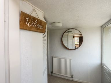 A hallway with a welcome sign a round wall mirror a radiator and a door at Ty Bedw in Benllech