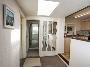 A hallway with three wavy mirrors on the wall and a doorway leading to a kitchen at Ty Bedw in Benllech