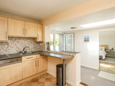 A kitchen with wooden cabinets a sink and a small breakfast bar opening to a bedroom at Ty Bedw in Benllech