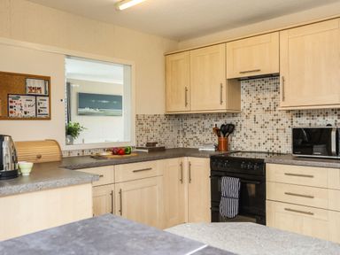 A kitchen with light wood cabinets black oven microwave and tiled backsplash at Ty Bedw in Benllech