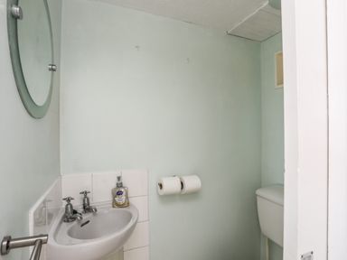 A small bathroom with a sink soap dispenser round mirror two toilet paper rolls and a toilet cistern at Ty Bedw in Benllech