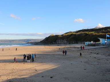 A sandy beach with people walking and playing near hills and a building by the sea at Ty Bedw in Benllech